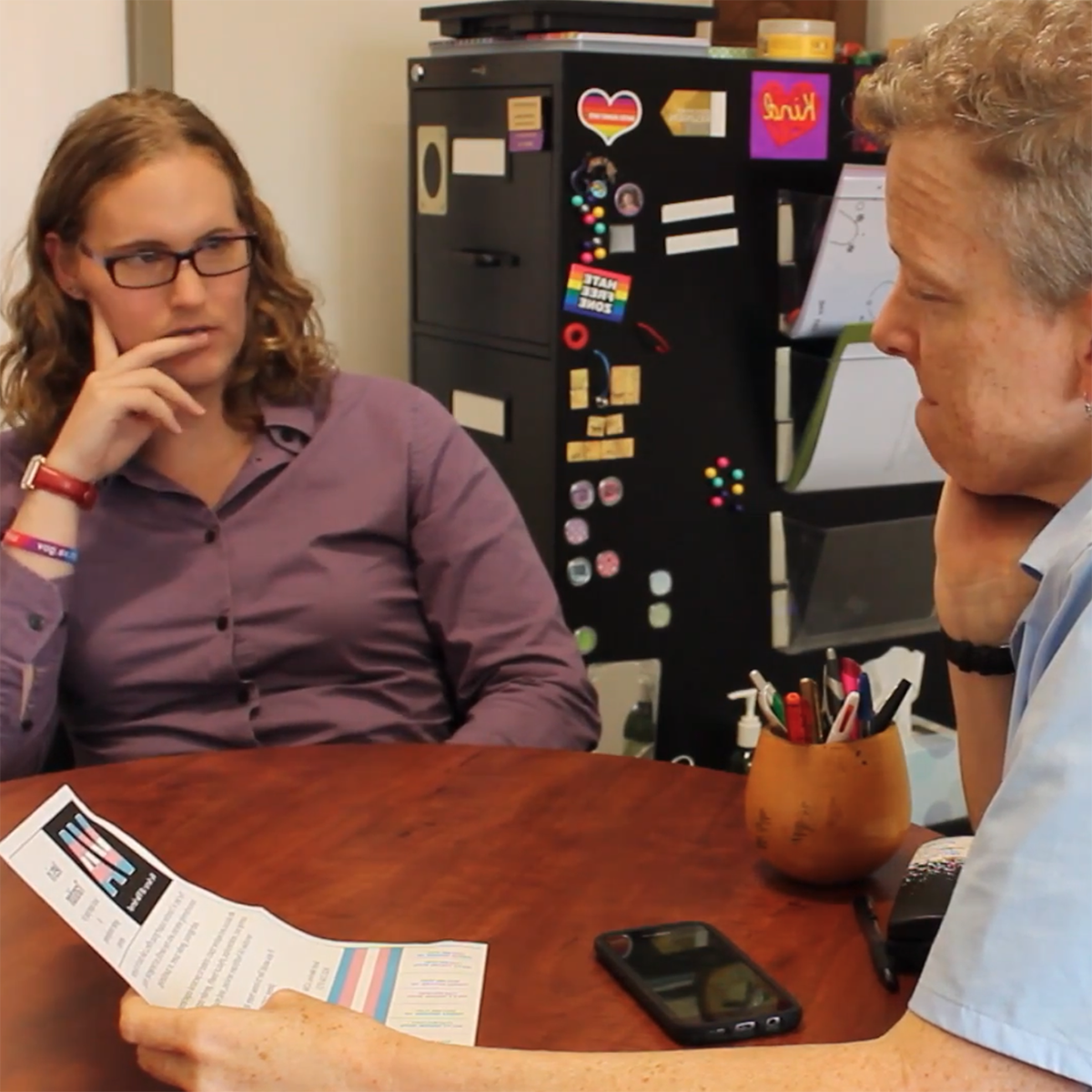 Photo of a student and professor Jen Morse speaking together in her office. 的re is a sticker in the background that says, HATE FREE ZONE